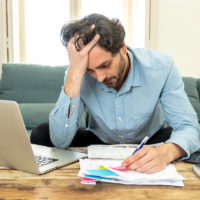 Angry man paying bills and debts in home with laptop and calculator