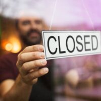 owner puts closed sign at bar or restaurant window