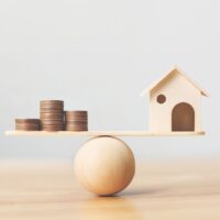 Wooden home and money coins stack on wood scale. Property investment and house mortgage financial real estate concept Wooden home and money coins stack on wood scale. Property investment and house mortgage financial real estate concept