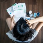 Top view of stressed young Asian woman hands holding the head trying to find money to pay credit card debt and all loan bills. Financial problem from coronavirus or covid-19 outbreak crisis concept.