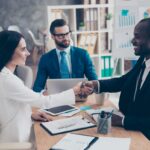 Partners making deal, shaking their hands, sitting in work place, wearing elegant, classic suits, to sign a contract, three professional, confident, stylish, attractive partners find a compromise