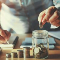 businessman saving money concept. hand holding coins putting in jug glass