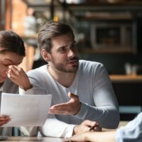 Angry young couple complaining, bad contract terms, outraged man arguing with manager or realtor, upset woman holding documents with stats, contract, dissatisfied clients demanding compensation