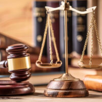 A judge’s gavel, a brass scale of justice, and legal books are arranged on a wooden table, symbolizing law and the judicial system. A judge’s gavel, a brass scale of justice, and legal books are arranged on a wooden table, symbolizing law and the judicial system.