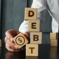 Debt is shown by wooden blocks with the word and the image of dollars. Payment of taxes and of debt to the state. Concept of financial crisis and problems. Risk management. Debt exemption and loan